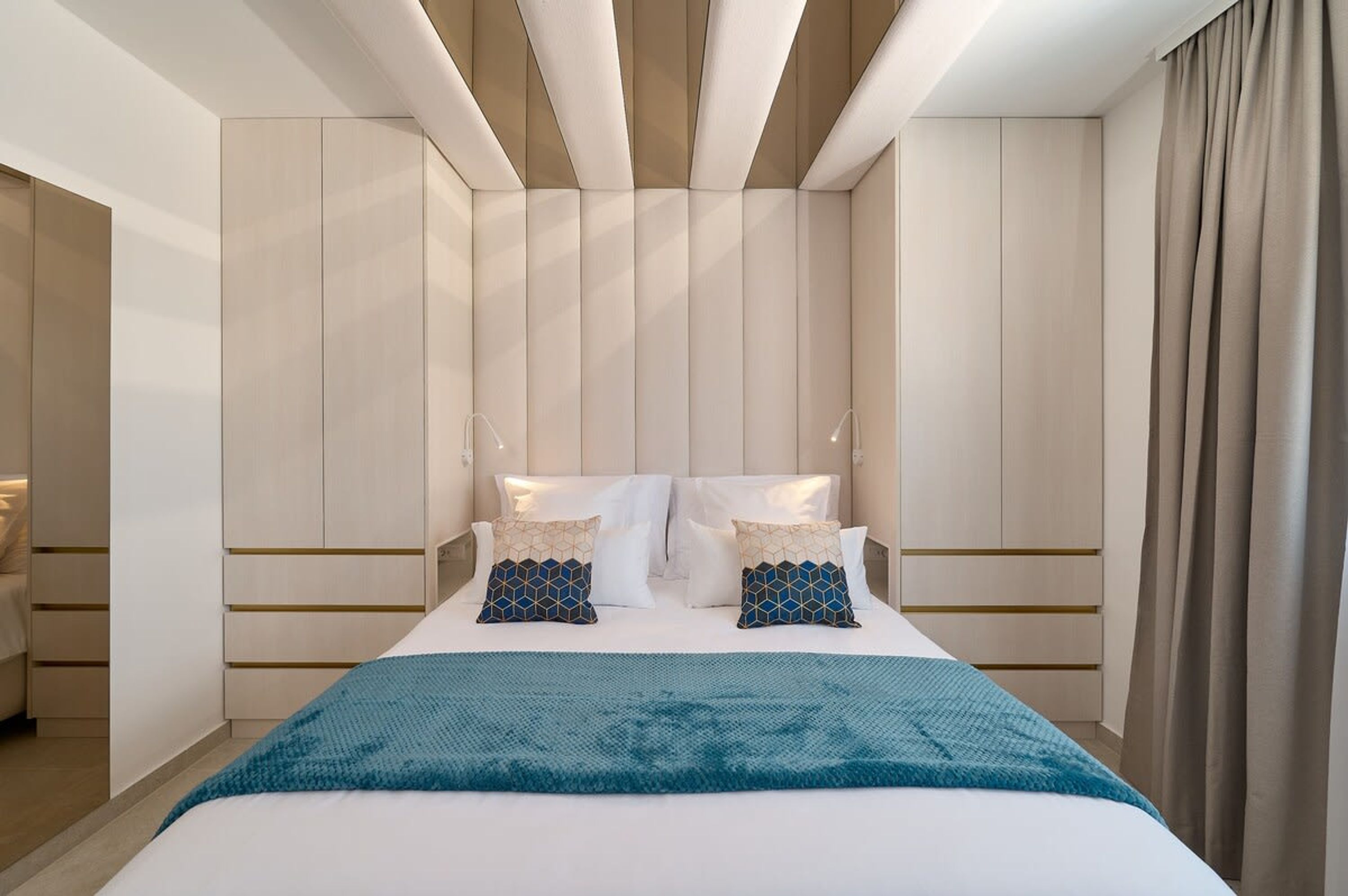 A modern hotel room with a large bed, a headboard with vertical lines, and a view of the city through the window.