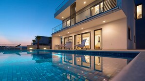 Una casa moderna con piscina, ventanas amplias y un balcón.