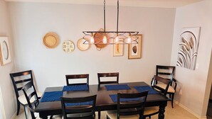 Un coin repas avec une table en bois foncé, six chaises et un luminaire suspendu.