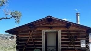 A rustic log cabin with a wooden door, a green chair outside, and a sign indicating 'Mule Parking Only'. - Rel Rio Rentals (Creede)