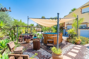 A patio area with a hot tub, wooden furniture, and potted plants.