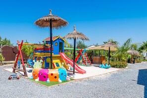 A playground with colorful play structures, including slides and climbing areas, surrounded by a gravel area and greenery. - Cubo's Villa Las Palmeras Altas Family / private pool / air conditioning / children's area / free wifi (Alhaurín el Grande)