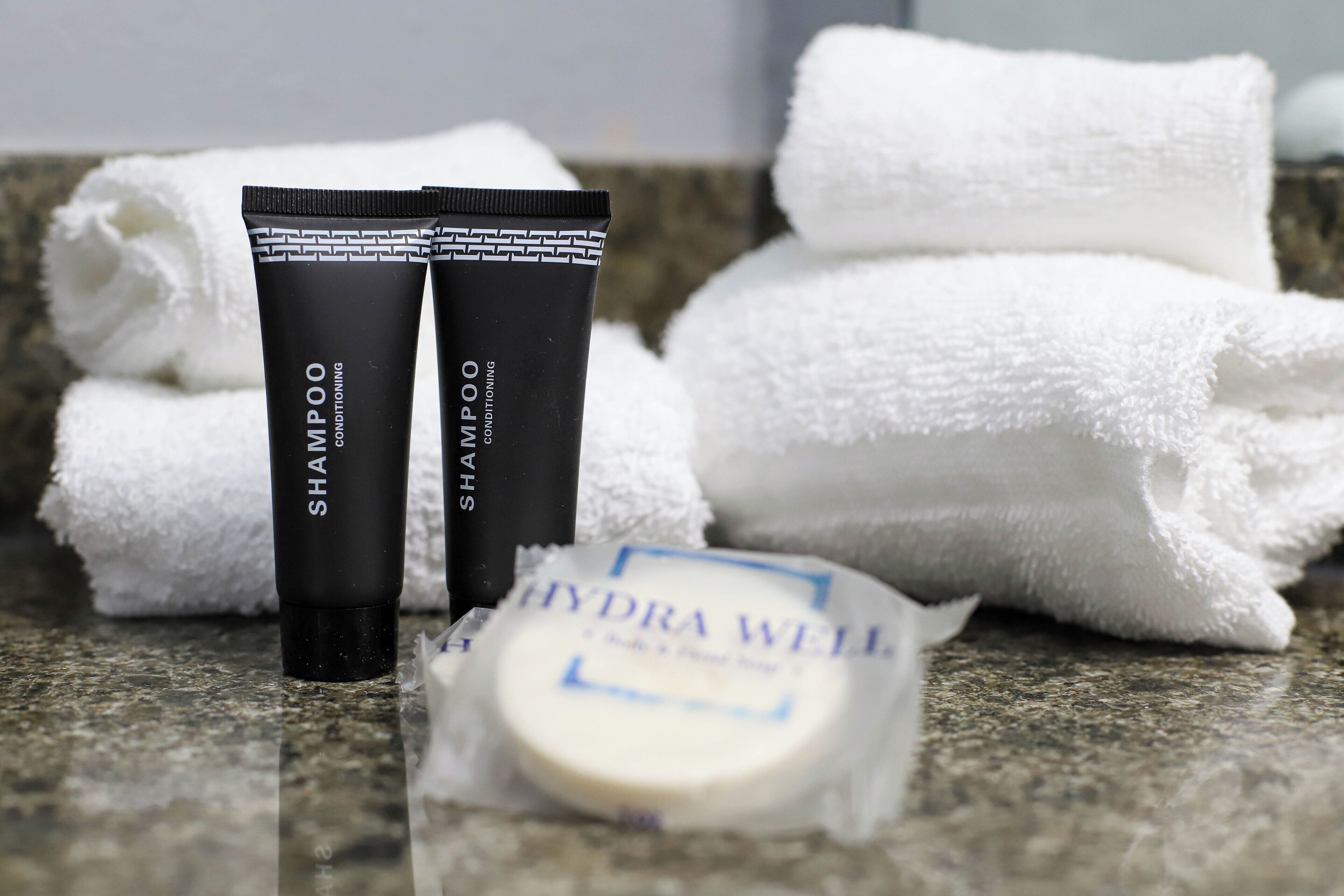 Two black tubes of shampoo and conditioner, a bar of soap, and white towels on a granite countertop.