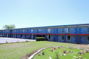 A motel with a row of rooms, a parking lot, and a landscaped garden area.