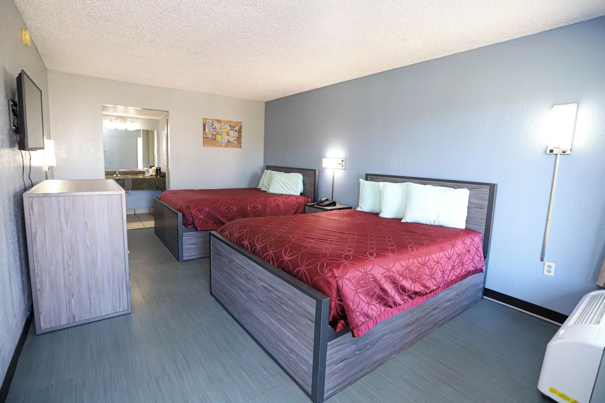 Habitación de hotel con dos camas, un tocador, un espejo y una lámpara en la pared.