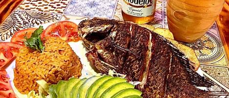 Une assiette contenant du poisson grillé, du riz, de l’avocat et des tranches de tomate.