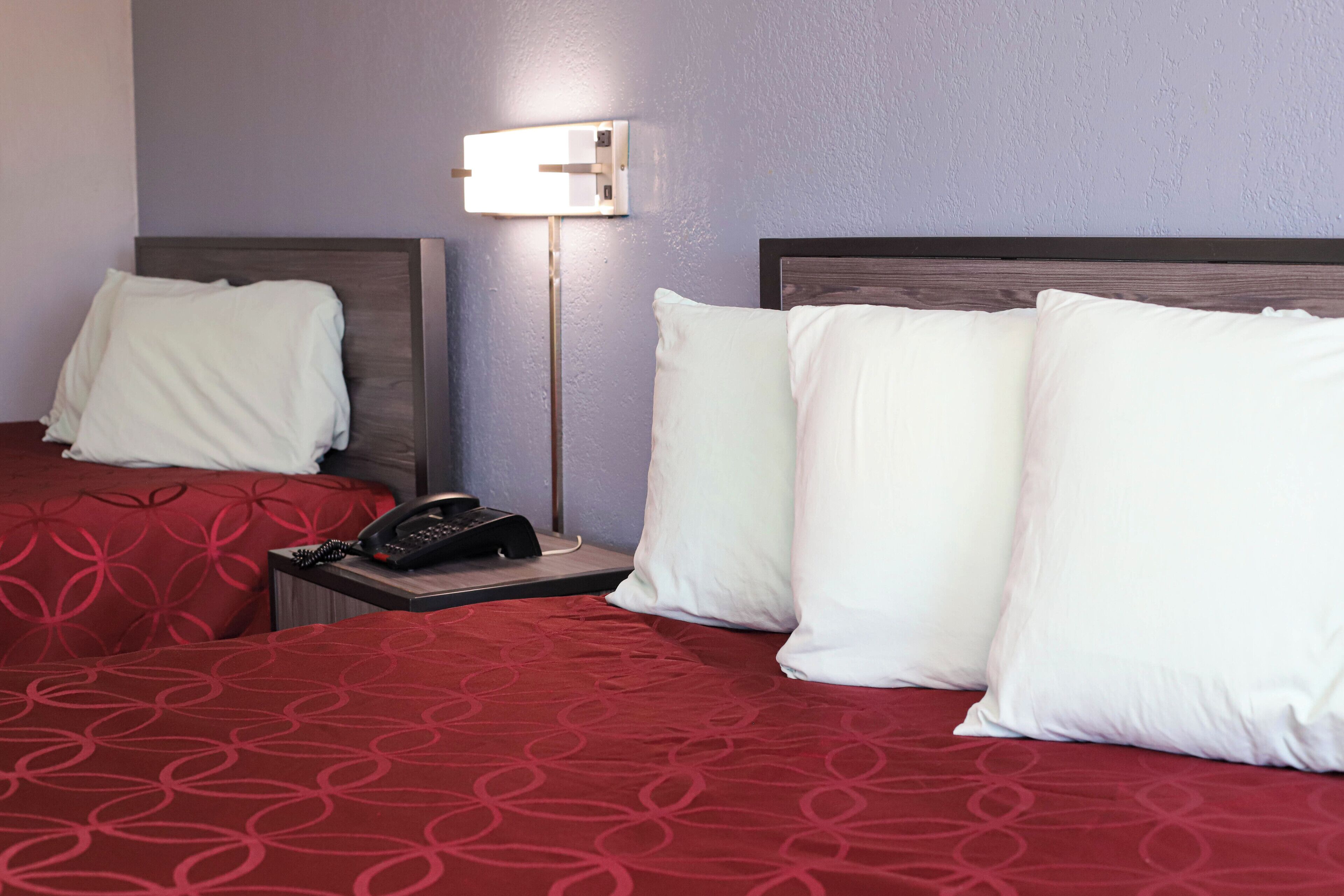 Une chambre d’hôtel avec deux lits, chacun recouvert d’une couvre-lit à motifs rouges et agrémenté d’oreillers blancs. On y trouve une table de chevet avec un téléphone et une lampe.