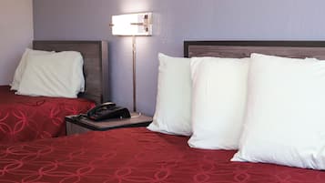 Een hotelkamer met twee bedden, elk voorzien van een rood beddegoed met een patroon en witte kussens. Er staat een nachtkastje met een telefoon en een lamp.