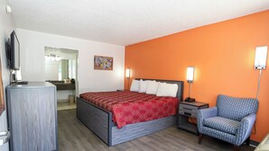 A hotel room with a bed, a desk, a chair, a TV, and a bathroom visible through an open door. - Express Inn  (Durant)