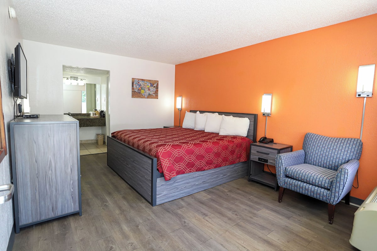 Una habitación de hotel con cama, escritorio, silla, televisor y baño visible a través de una puerta abierta.