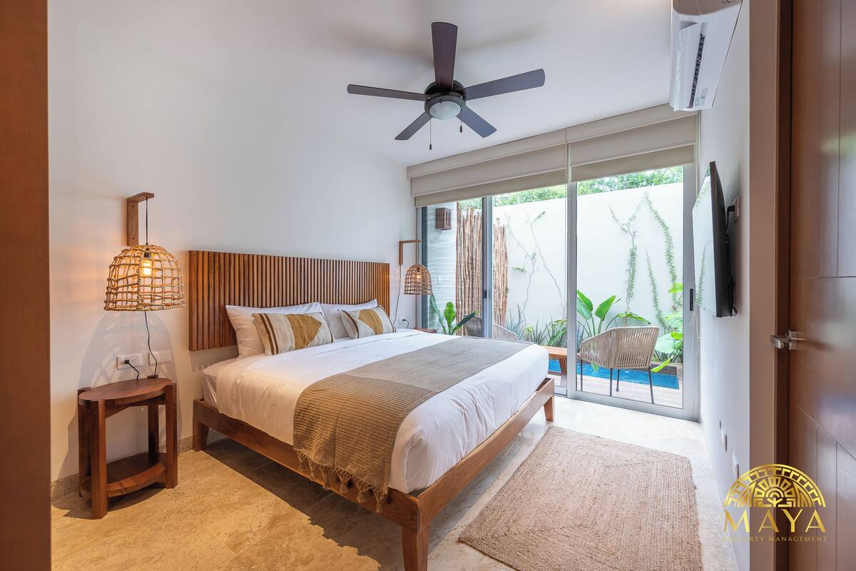 Quarto com cama, luminária de cabeceira, ventilador de teto e vista para o exterior por uma porta de vidro deslizante.