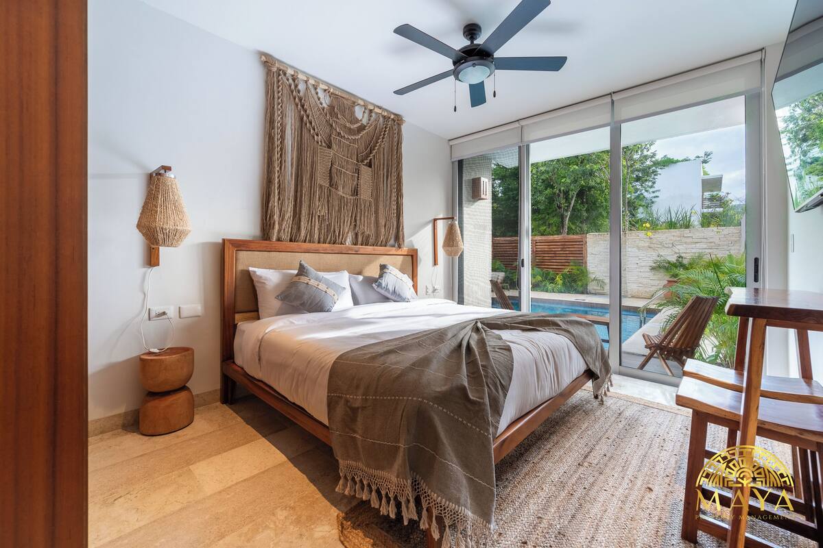 Quarto com cama, ventoinha no teto, janela grande e vista para o exterior.