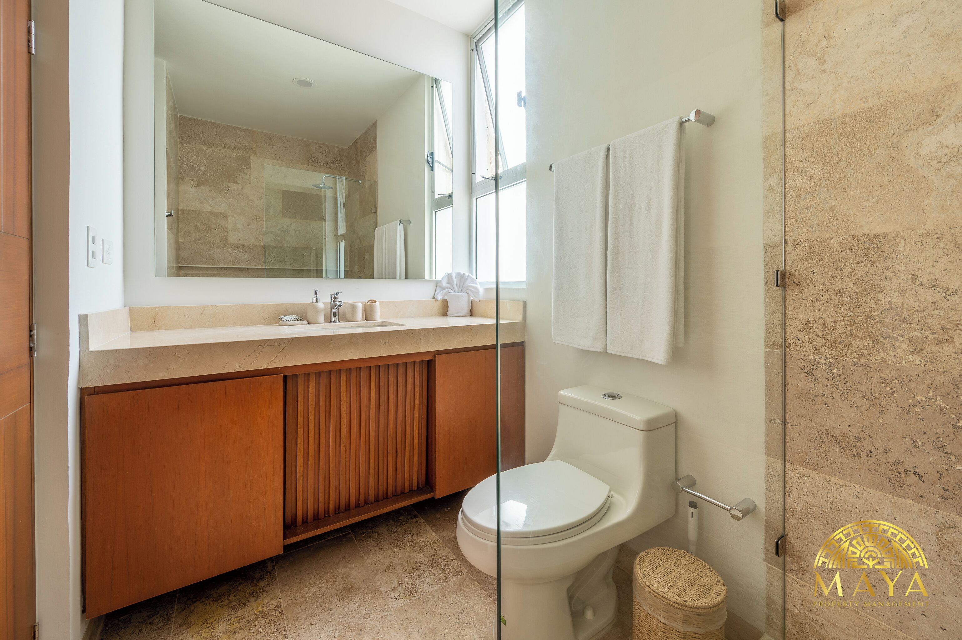 A modern bathroom with a glass shower enclosure, a wooden vanity, a toilet, and a large mirror.