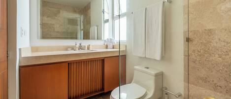 A modern bathroom with a glass shower enclosure, a wooden vanity, a toilet, and a large mirror.