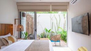A bedroom with a large bed, a TV mounted on the wall, and a sliding glass door leading to a balcony with plants. - NHOA TULUM APARTHOTEL by Maya PM (Tulum)