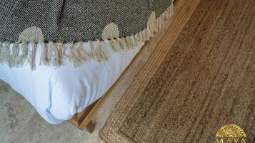 A bed with a white sheet and a grey blanket with a fringe.