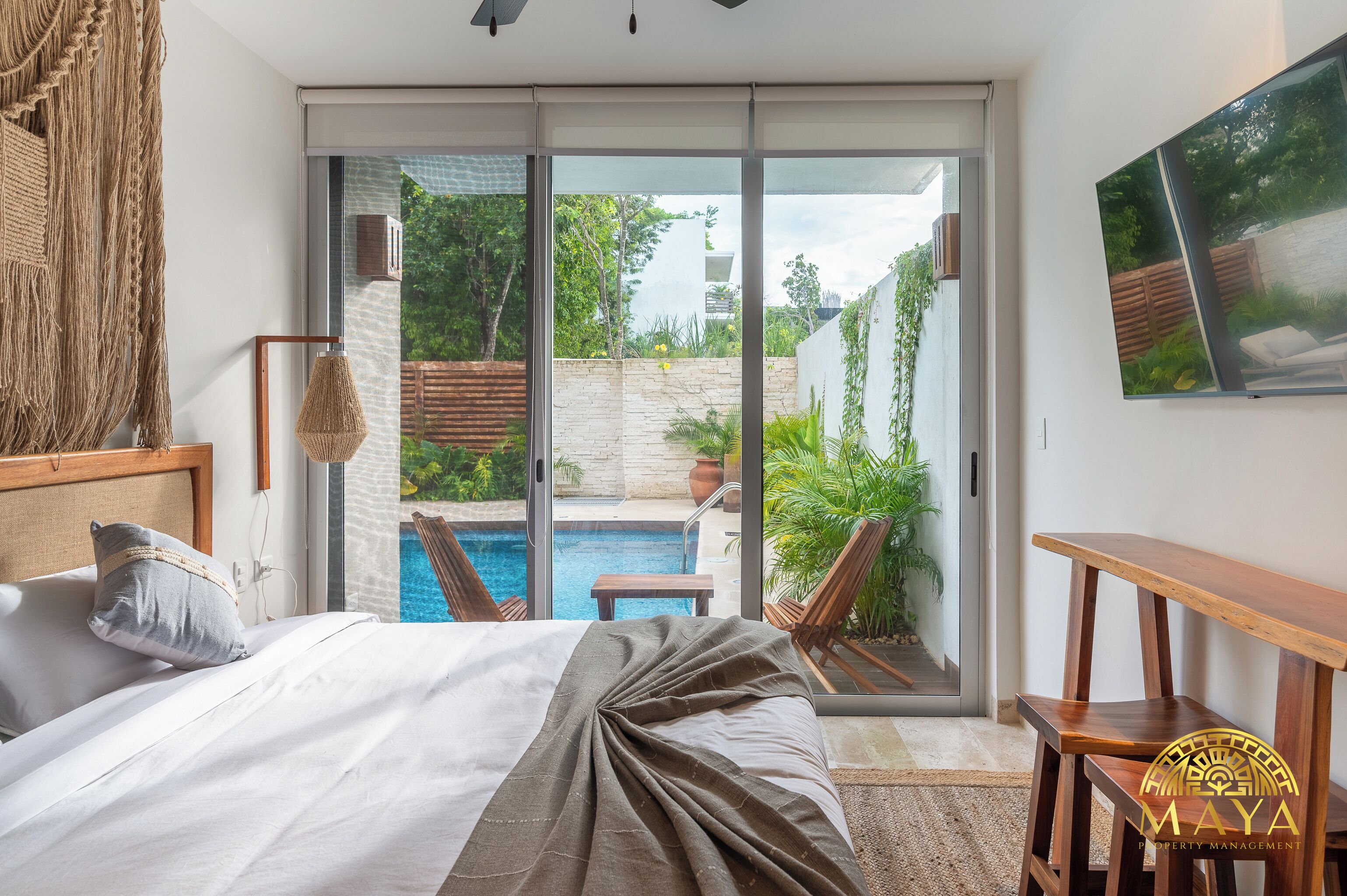 A bedroom with a large bed, a view of a swimming pool, and a wooden bench.
