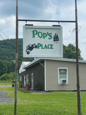 Un cartello con su scritto 'Pop's Place' e una casa sullo sfondo.