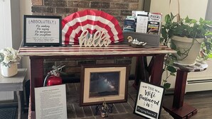 Una reception con una bandiera americana incorniciata, un cartello con la scritta 'Hello', un cartello 'Vietato fumare', un estintore, un quadro incorniciato e cartelli informativi su WiFi e piano antincendio.