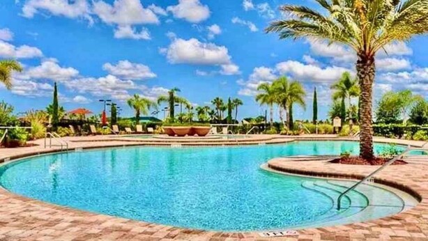 Une piscine avec une terrasse carrelée, des palmiers et un ciel bleu azur.