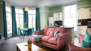 A living room with a pink sofa, teal curtains, and a dining area with blue chairs. - This apartment is a 2 bedroom(s), 1 bathrooms, located in Scarborough, North Yorkshire. (Scarborough)