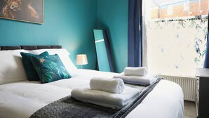 A hotel room with a large bed, teal walls, a painting, and a window with curtains. - This apartment is a 2 bedroom(s), 1 bathrooms, located in Scarborough, North Yorkshire. (Scarborough)