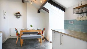 Una cocina moderna con una mesa de comedor de madera, sillas y un banco empotrado. Hay una ventana que proporciona luz natural y una estantería con utensilios de cocina.