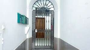 A hallway with a decorative metal gate, a wooden door, and a green electrical box on the wall. - Apartment in the center of Sanlúcar (Sanlúcar de Barrameda)