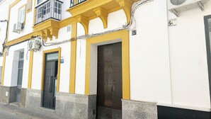A building with a yellow facade, a black door, and a balcony with a metal railing. - Apartment in the center of Sanlúcar (Sanlúcar de Barrameda)