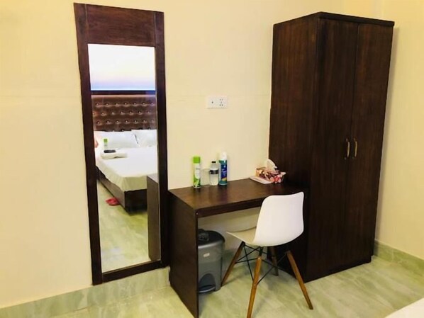 A hotel room with a bed, a desk with a chair, a wardrobe, and a trash bin. - Cafe Green Valley (Rangpur)