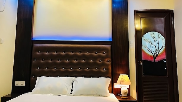 A neatly made bed with white linens, a tufted headboard, and a bedside lamp. - Cafe Green Valley (Rangpur)