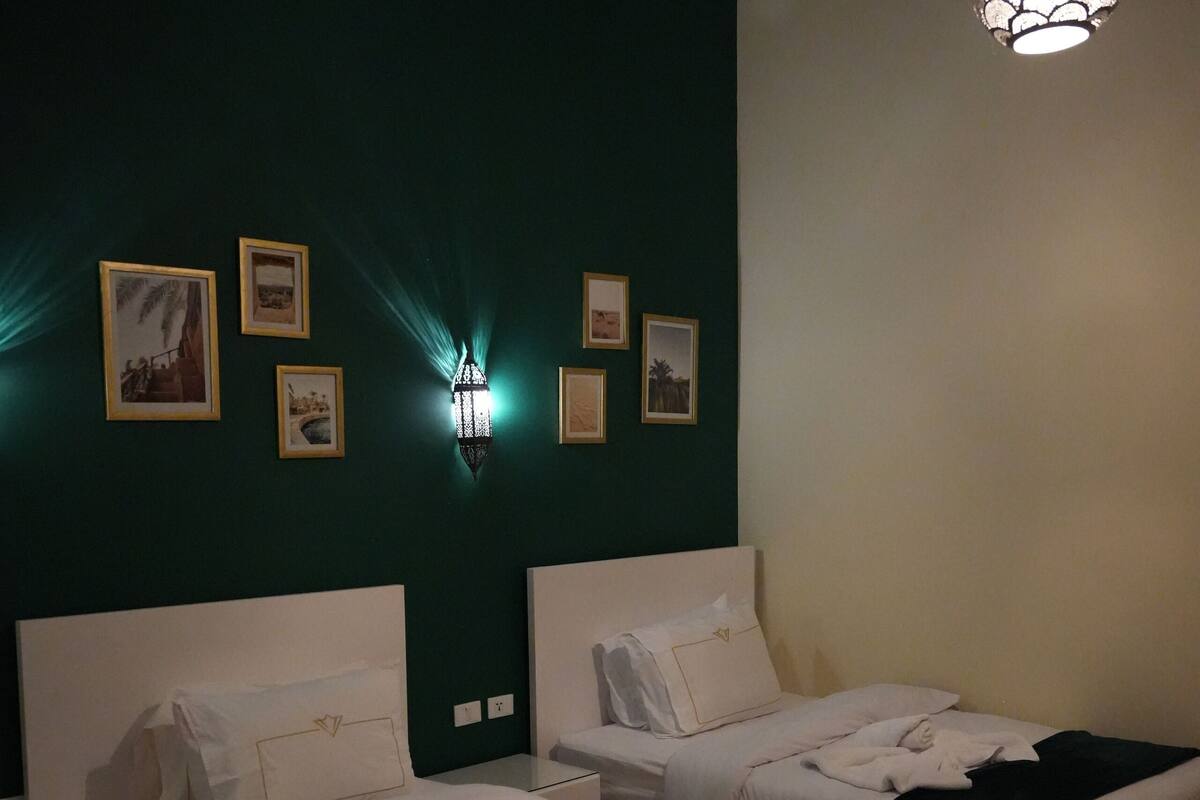 Habitación de hotel con dos camas, una lámpara fijada a la pared y cuadros enmarcados.