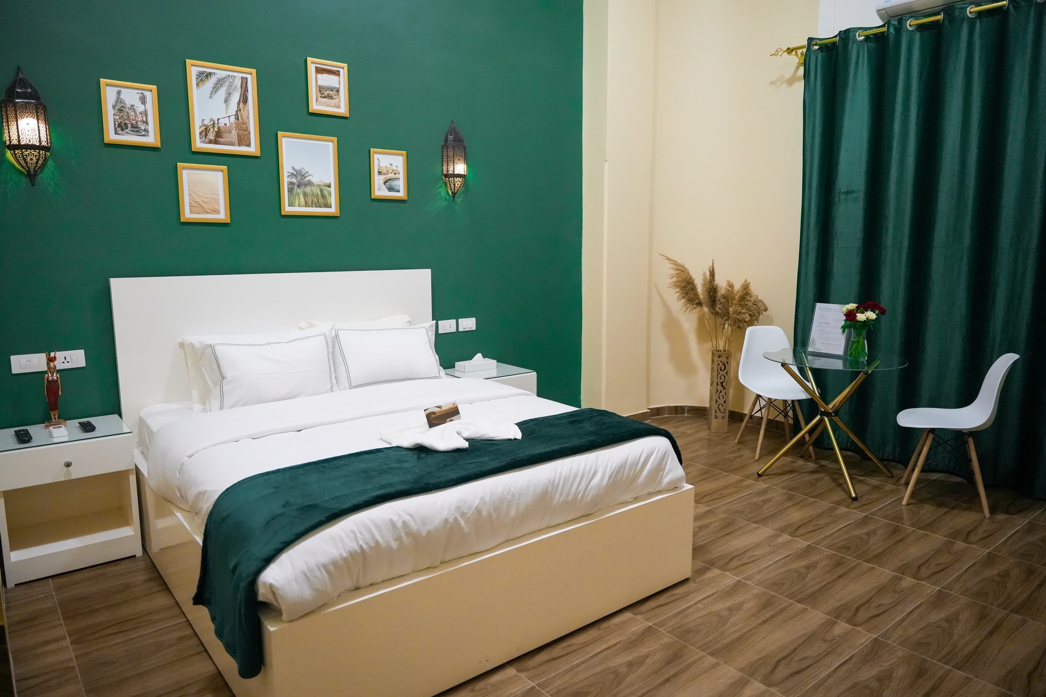 A neatly arranged bedroom with a large bed, bedside tables, a small table with chairs, and wall-mounted picture frames.
