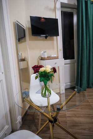 A glass table with a vase of flowers, a white chair, a television on the wall, and a green curtain. - Hathor House (Cairo)