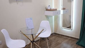 A small room with a round glass table, two white chairs, a flat-screen TV, a mirror with lights, and a small shelf with toiletries. - Hathor House (Cairo)