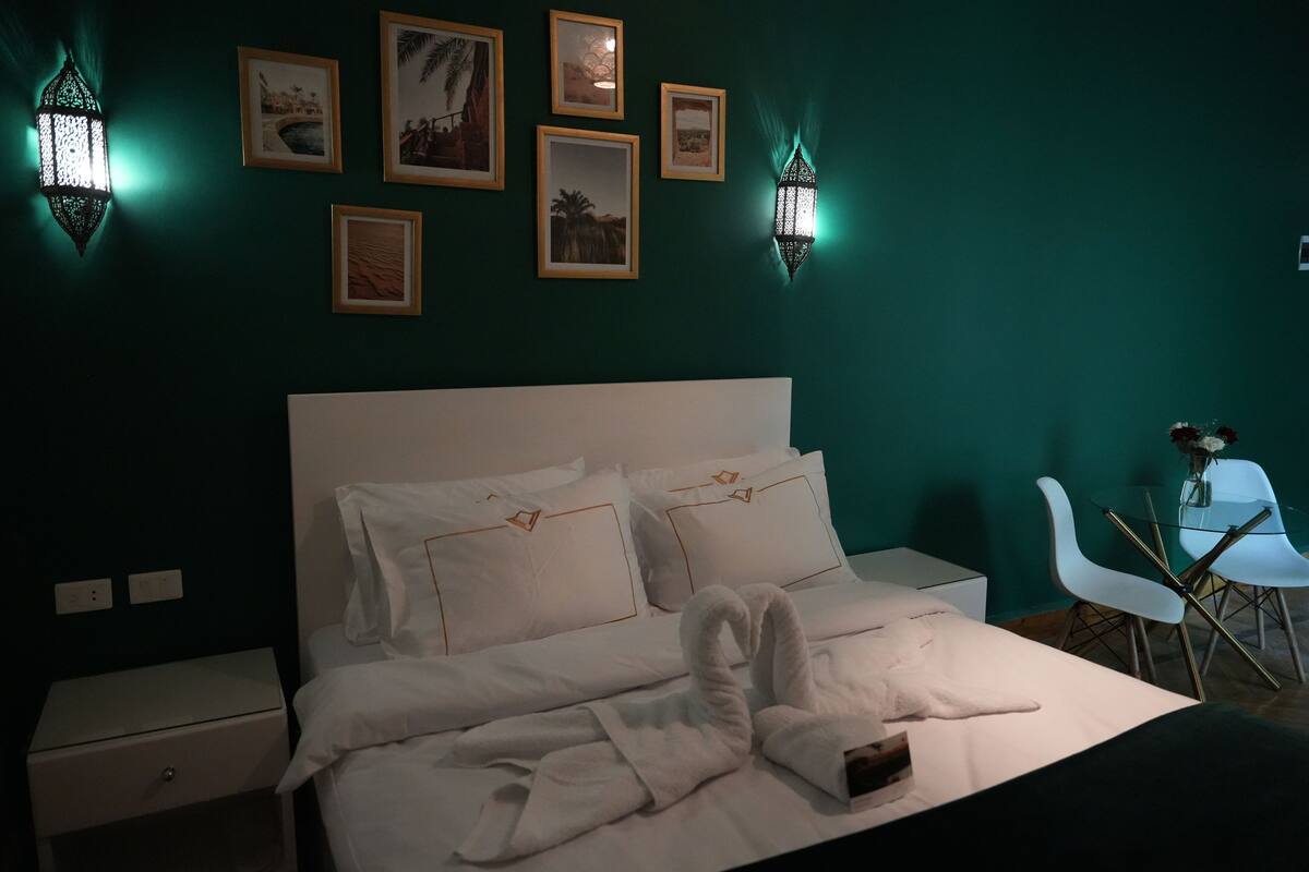 Una habitación de hotel con una cama grande, ropa de cama blanca y un conjunto de cuadros colgados en la pared.