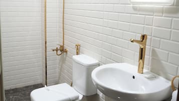 A bathroom with white subway tiles, a white toilet, a white sink with gold fixtures, and a shower with gold fixtures.