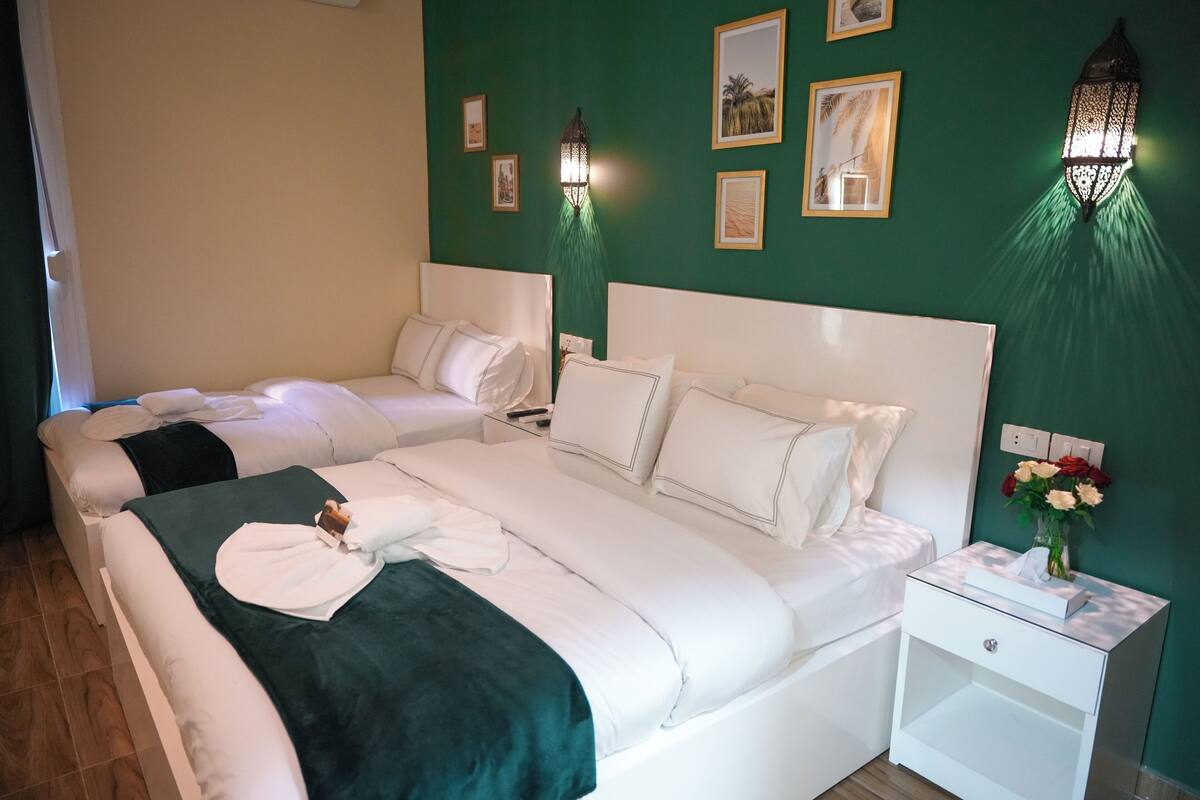 Habitación de hotel con dos camas, una pared verde y apliques decorativos.