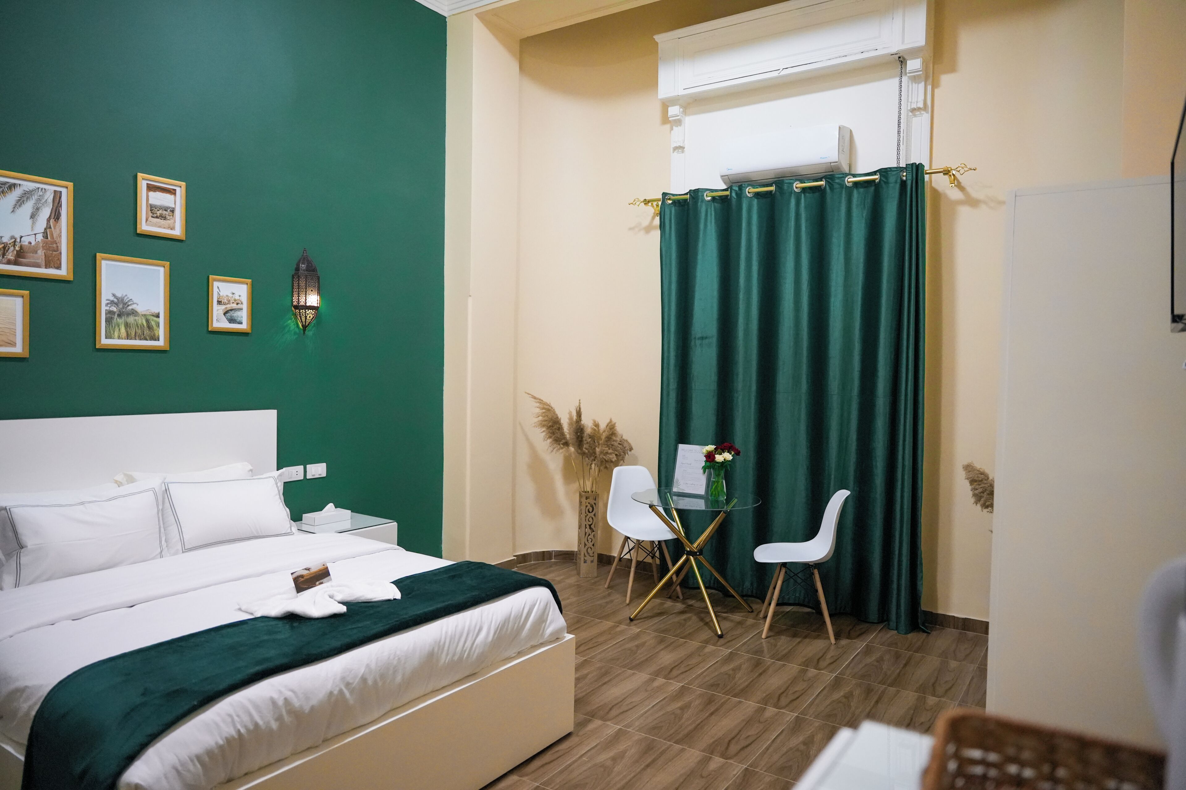 Une chambre d’hôtel avec un lit, un bureau, des chaises, un rideau vert et des lampes fixées au mur.