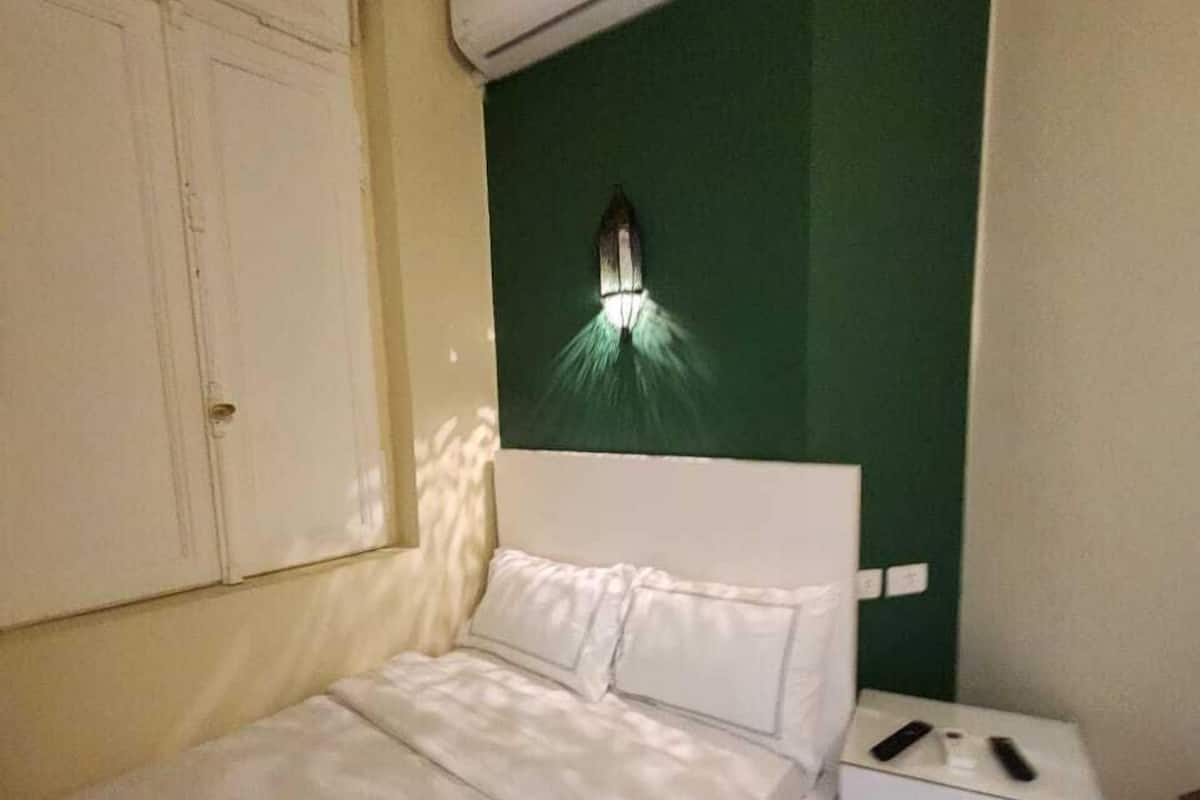 Un dormitorio con una cama, una mesita de noche, un aire acondicionado de pared y una lámpara de pared.