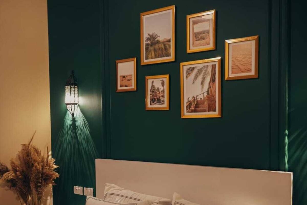 Un dormitorio con una cama grande, una mesita de noche, una lámpara de pared y cuadros enmarcados.