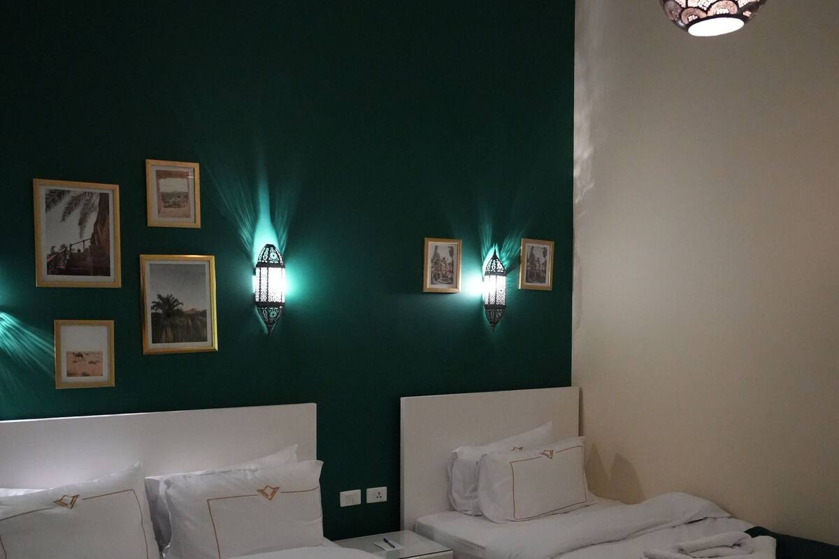 Habitación de hotel con dos camas, suelo de madera y lámparas fijadas a la pared.