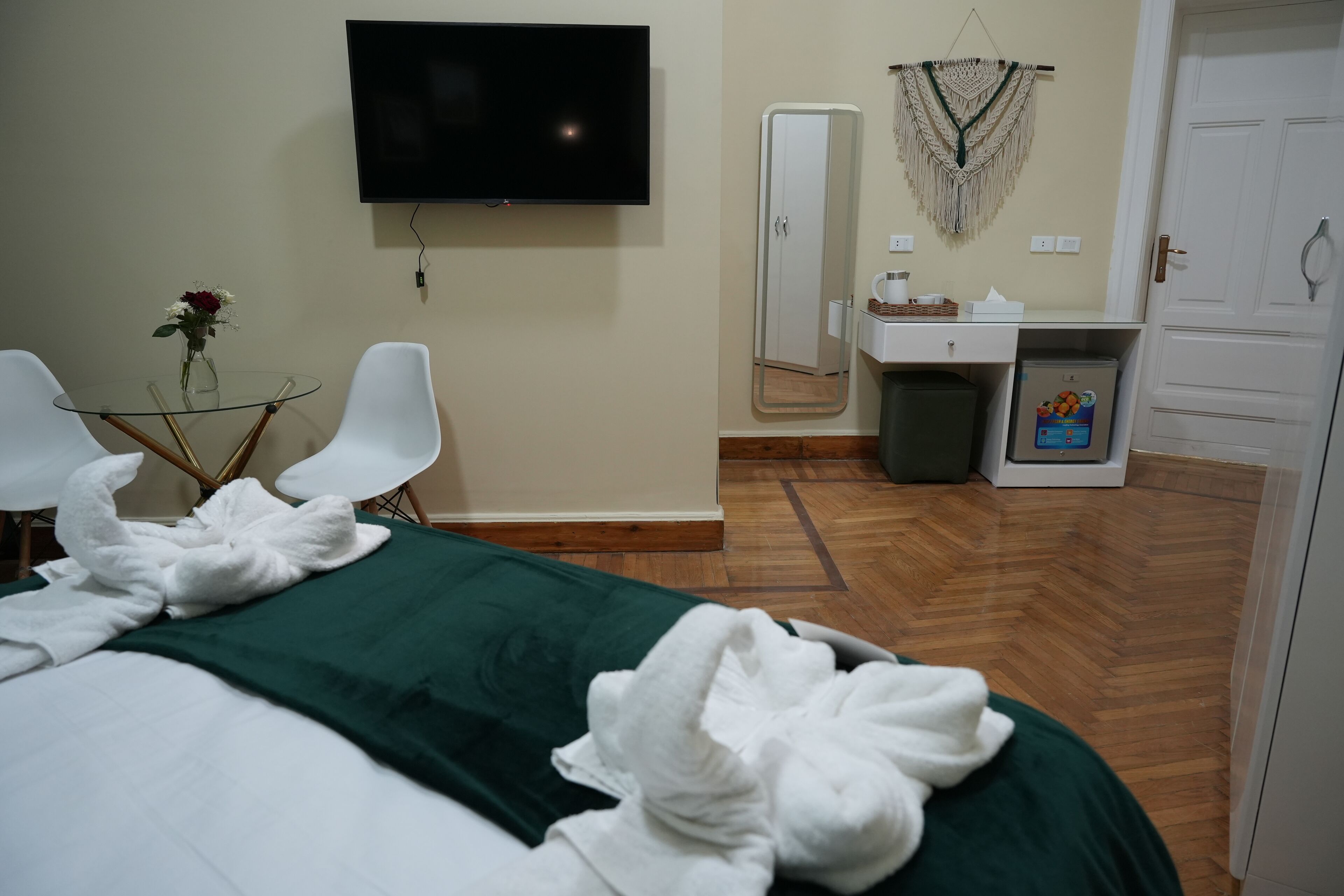 A hotel room with a bed, a TV, a small table with a vase, a mirror, and a wardrobe.