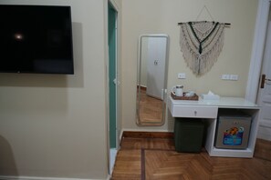 A room with a flat-screen TV, a mirror, a sink, a trash bin, and a mini-fridge. - Hathor House (Cairo)