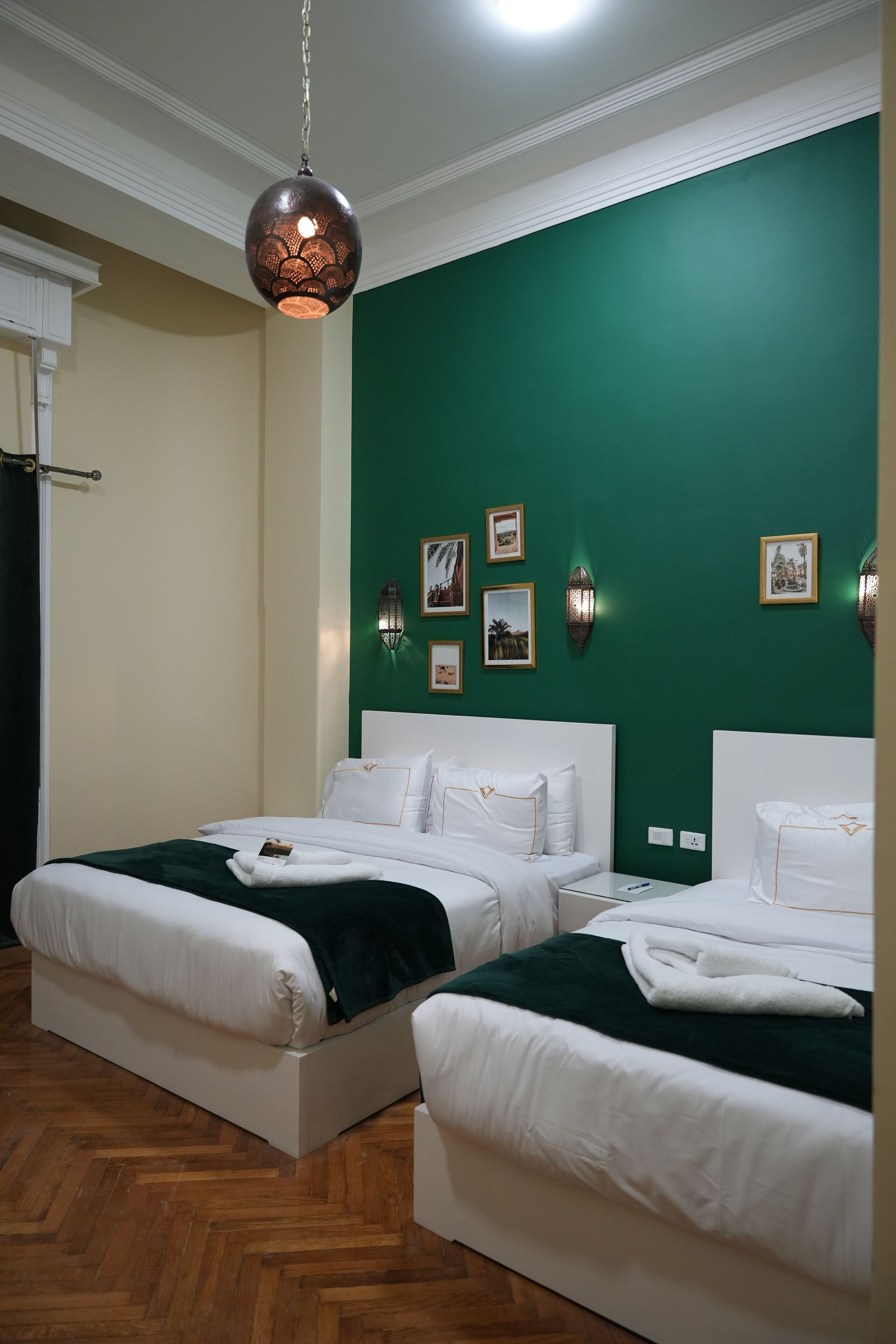 A hotel room with two beds, a green accent wall, and wall-mounted picture frames.