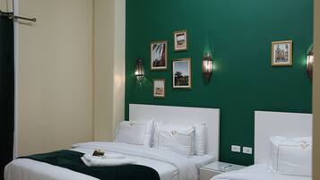A hotel room with two beds, a green accent wall, and wall-mounted picture frames.