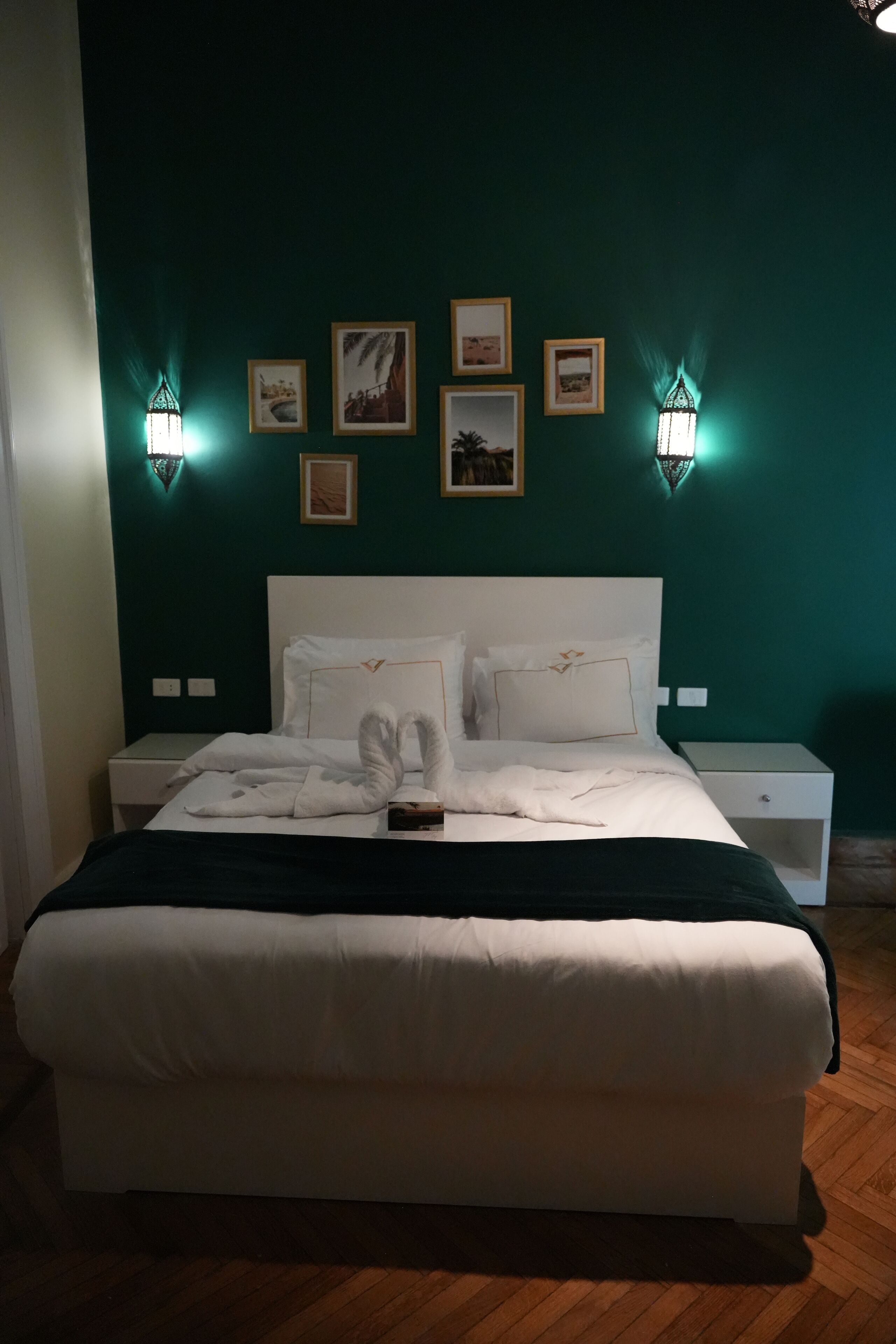 A neatly made bed with white linens and towels, two bedside tables, and wall-mounted lights.