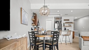 A modern kitchen with a dining area, featuring a wooden dining table, black chairs, and a chandelier. - Stunning Newly Renovated Poolside Condo Near Beach. Now With Beach Service! (Miramar Beach)