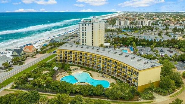 A hotel with a pool, beachfront view, and multiple buildings in the background. - Stunning Newly Renovated Poolside Condo Near Beach. Now With Beach Service! (Miramar Beach)