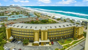 A hotel with a curved facade, multiple floors, and a parking lot in front. - Stunning Newly Renovated Poolside Condo Near Beach. Now With Beach Service! (Miramar Beach)